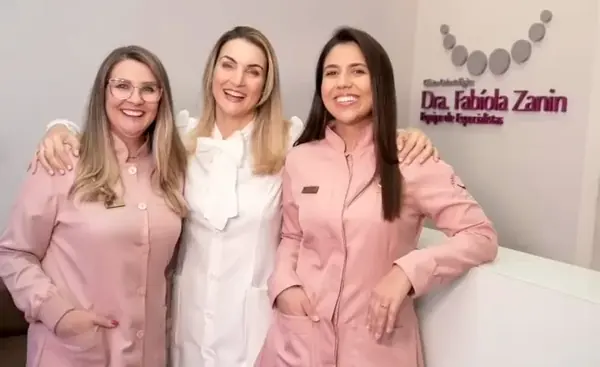 Três profissionais da equipe na recepção, em frente ao logo da clínica